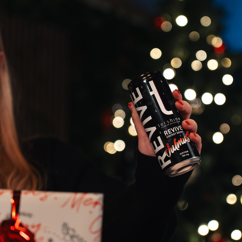 En person håller en burk Tershine Revive - Julmust framför en julgran.