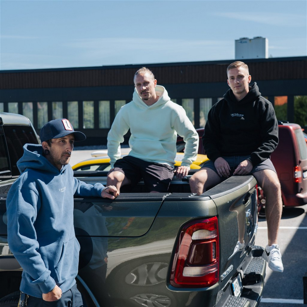 Tre män sitter på en truck, iklädda hoodies i olika färger.