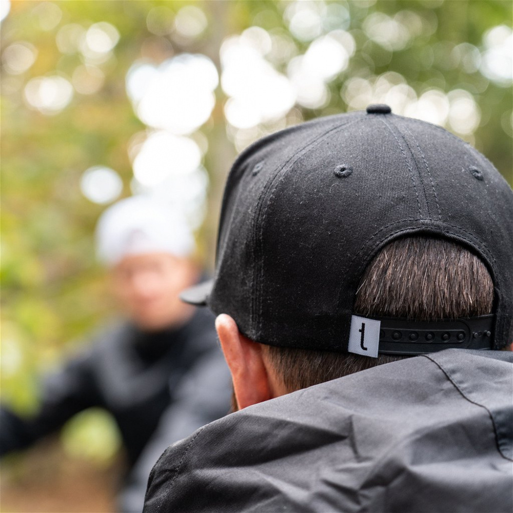 En person med svart snapback-keps, suddig bakgrund och skogsmiljö.