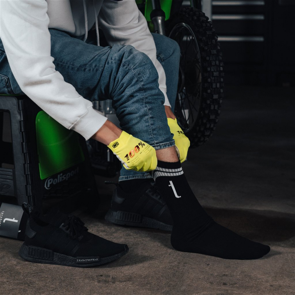 En person tar på sig svarta strumpor med en vit logotyp.