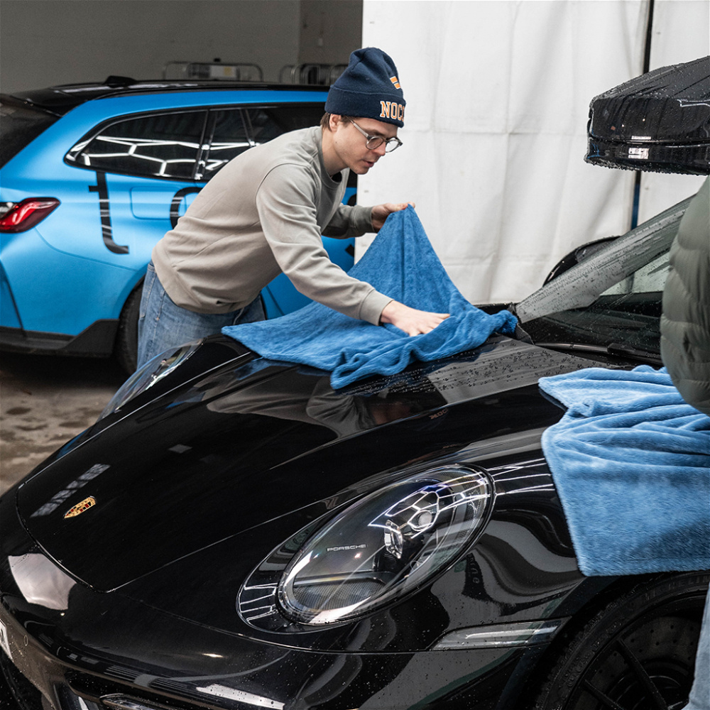 En person torkar en svart bil med en blå torkduk i en garagemiljö.