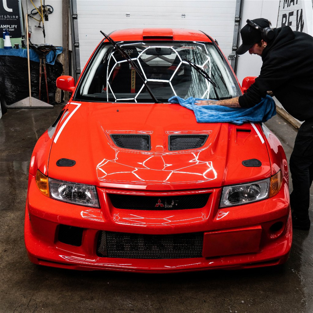 En man torkar en röd bil med en blå torkduk i en garage miljö.