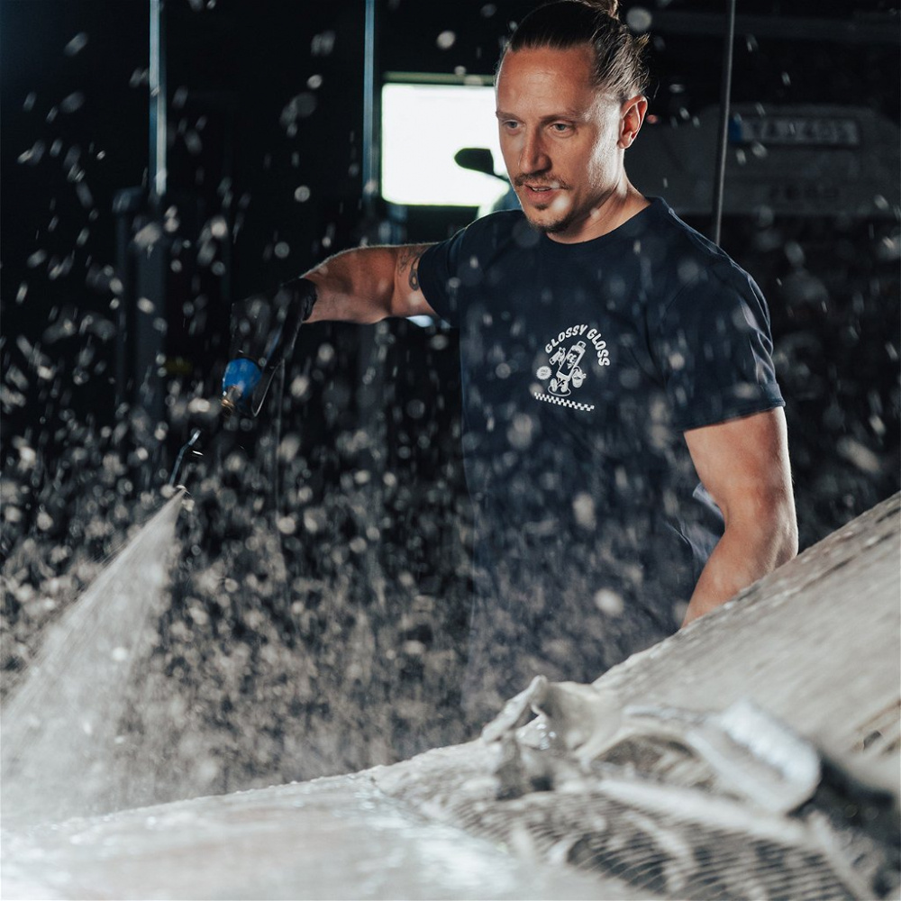 En man i T-shirt sprutar vatten på en yta, med skum och droppar runtom.