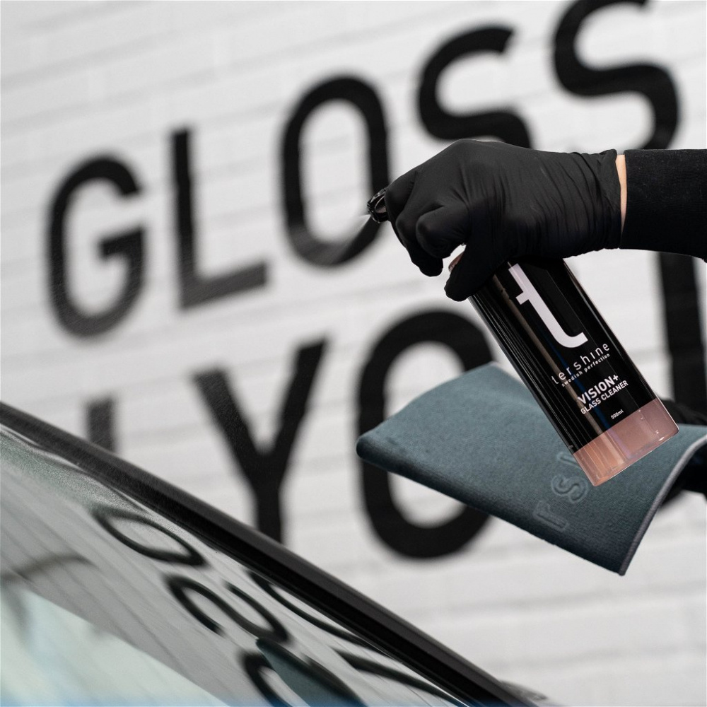 En hand sprayar Tershine Vision+ glasrengöring på en bilruta med en mikrofiberduk.