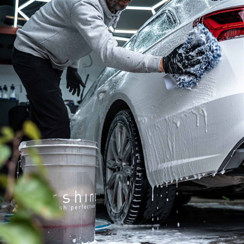 En person tvättar en bil med en tvätthandske i en garage.