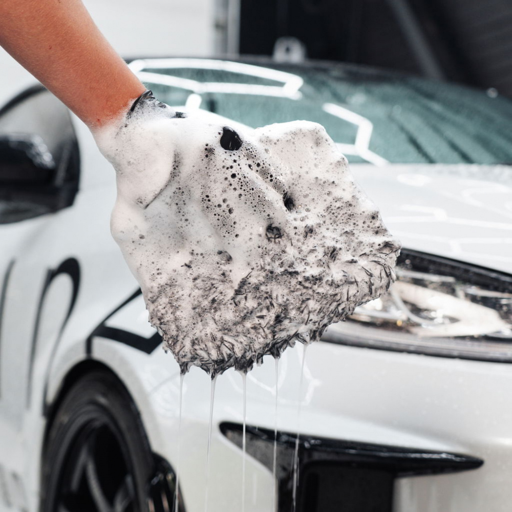 En hand med en tvättsvamp i skum, nära en bil.