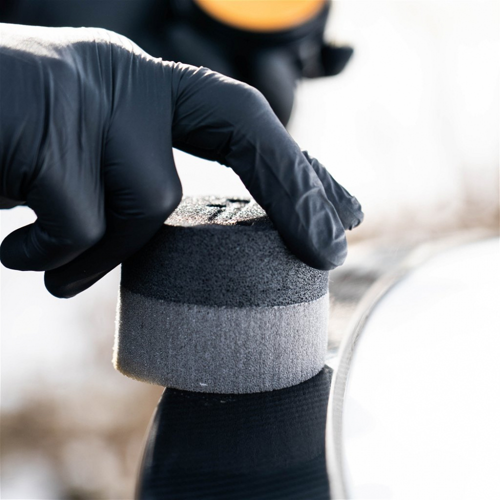 En handske håller en vax-applikator mot en bils yta.