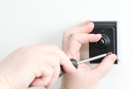 En person installerar en svart hållare på en vägg med en skruvmejsel.