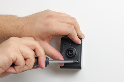 En hand skruvar fast en svart hållare på en vägg.