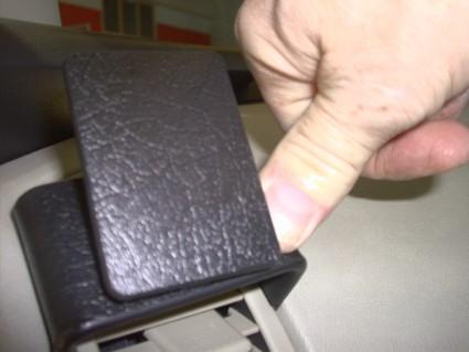 En hand trycker på en svart plastdetalj i en bil.