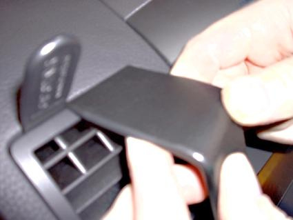 En hand tar bort en svart plastdel från en bilpanel.