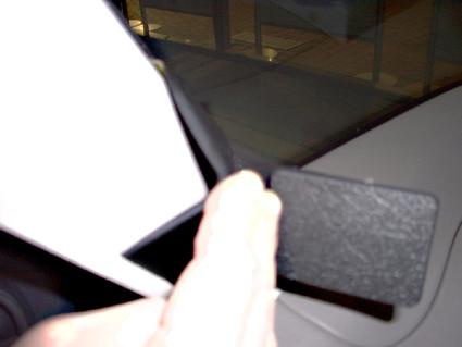 En hand håller en svart del nära bilfönstret.