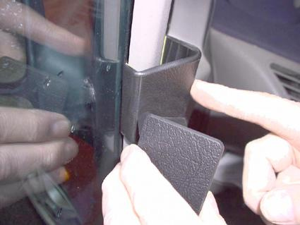 En hand som visar en svart plastdel vid en bils dörr.