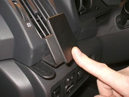 En pekfinger trycker på en svart enhet i en bils ventilationssystem.