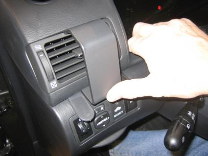 En hand justerar kontroller på en bils mittkonsol, troligen för ventilation och säkerhet.