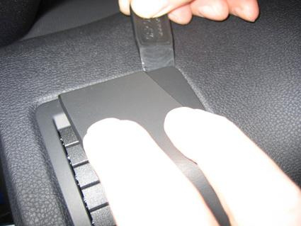 En hand använder ett verktyg för att ta bort en panel i bilen.