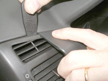 En hand tar bort en plastdel vid bilens luftventil.