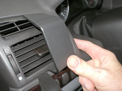 En hand håller i en del av instrumentpanelen vid luftventilen.