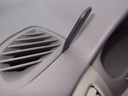 En del av en bilinteriör med ventilationsgaller och en liten spak.