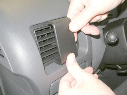 En hand tar bort en ventilationsgallerpanel från en bil.