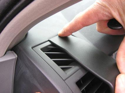 En hand pekar på en panel nära luftutloppet i en bil.
