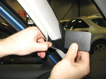 En person tar bort klistermärke från bilens A-stolpe.