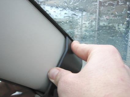 En hand håller i solenheten nära ett fönster med regn.