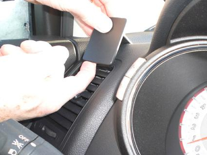 En hand placerar en platt svart del på instrumentbrädan i en bil.