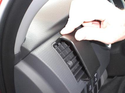 En hand pekar på en del av bilens inredning, troligtvis en luftventil.