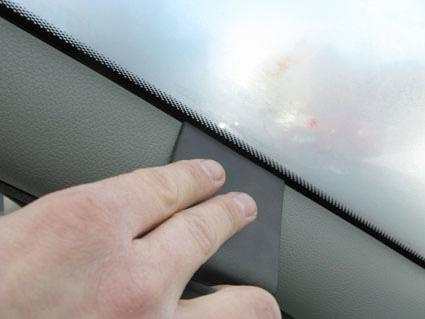 En hand trycker på en tätning vid fönstrets kant i en bil.