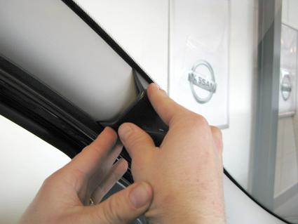 En hand fäster en del vid bilens fönsterbåge.