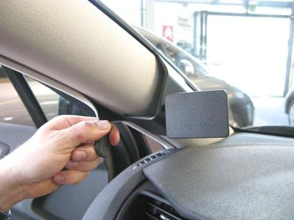 En hand fäster något på en bils interiör, nära spegeln.