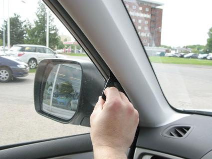 En hand som justerar eller tar bort en del vid bilens vänstra fönster.