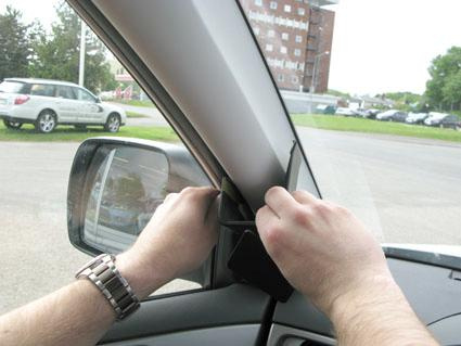 Två händer installerar en del vid bilens vindruta.