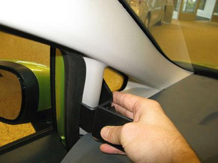 Hand som håller ett svart föremål vid bilens A-stolpe.