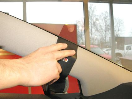 En hand som installerar något på bilens vänstra A-stolpe.