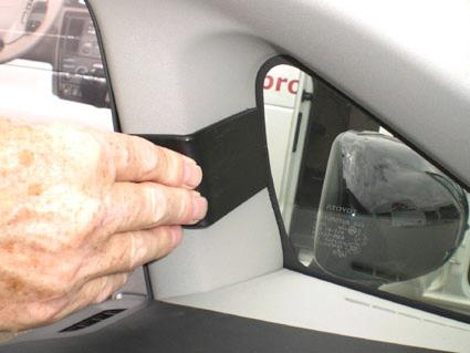 En hand fäster en svart komponent vid bilens vänstra sidospegel.