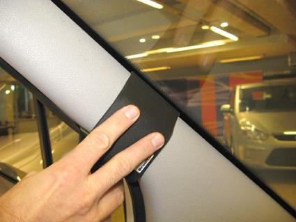 En hand håller i en svart del vid bilens vänstra vindruta.