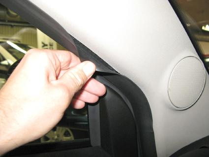 En hand lyfter en gummilisten i en bilinteriör.