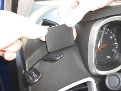 En person fäster en svart plastbit på instrumentbrädan i en bil.