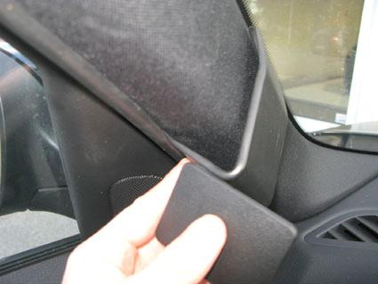 En hand som håller i en svart del av bilens interiör, nära vindrutekanten.