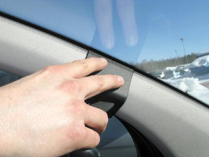 En hand trycker på ett gummiliknande remsa vid bilens fönsterkarm.