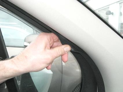 Hand som justerar en gummitätning vid en bilruta.
