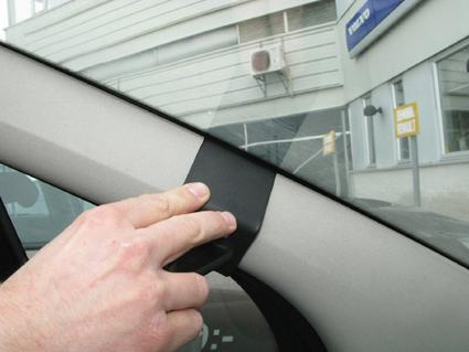 En hand håller i ett svart plaststycke på bilens innerfönster.