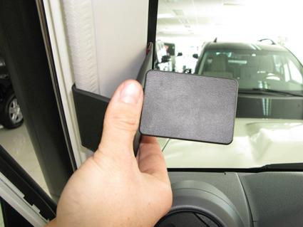 En hand håller en svart rektangulär del vid bilens dörr.