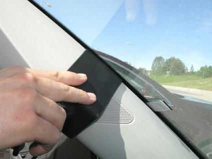 En hand som håller en svart del vid vindrutan i en bil.