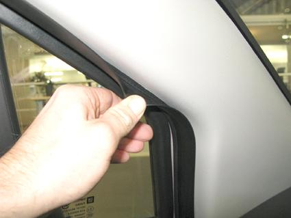 En hand håller i en svart gummilist vid en bils dörr.
