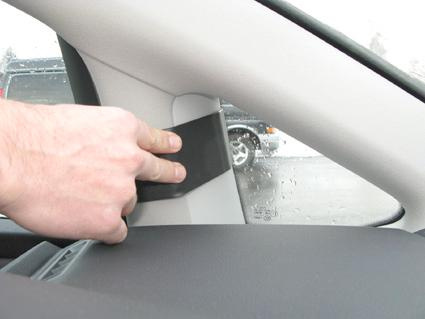 En hand som tar bort en svart panel från en bils inredning.