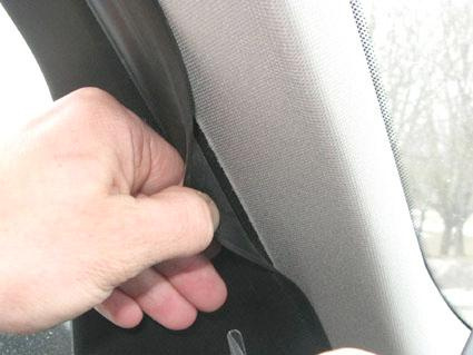 En hand drar i en svart trimdel vid en bilfönsterkant.