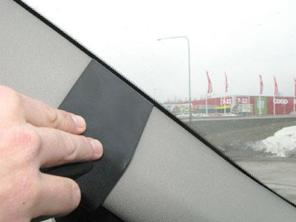 En hand fäster svart material på en bils inre sidokärna.